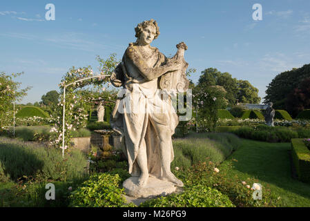 Una statua di pietra di un lettore per liuto e ricoperto di rose arcate nel parterre di rose nel giardino murato a Houghton Hall in King's Lynn, Norfolk, Regno Unito Foto Stock