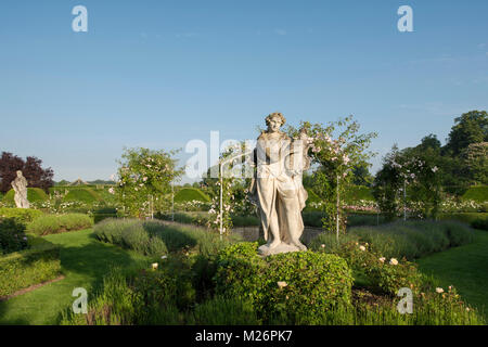 Una antica statua di pietra di un musicista e Rosa "Cecile Brunner' su archi nel parterre di rose a Houghton Hall, King's Lynn, Norfolk, Regno Unito Foto Stock