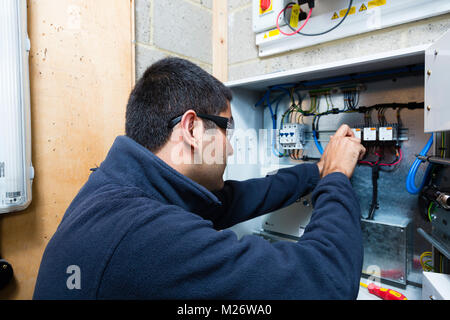 Un giovane Asian apprendista elettricista lavora con un cacciavite in una scatola di giunzione. Foto Stock