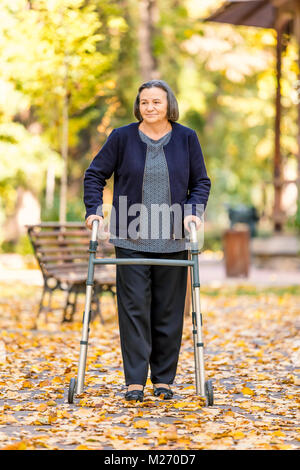 Senior donna con walker passeggiate all'aperto nel parco d'autunno. Foto Stock