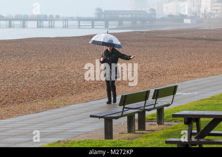 Una donna con un ombrello a piedi sotto la pioggia sul lungomare di Hastings, east sussex, Regno Unito Foto Stock