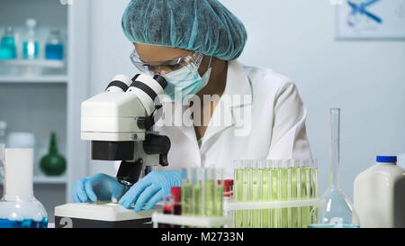 Donna scienziato che guarda nel microscopio, ricerche biochimiche, cosmetologia Foto Stock