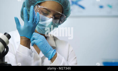 Ragazza Biracial mettere dei guanti di protezione in lattice in laboratorio, la preparazione per la ricerca Foto Stock