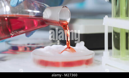 Close-up di ricercatore del laboratorio la mano di versamento liquido rosso in vetreria, cosmetologia Foto Stock