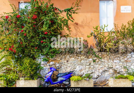 Uno scooter parcheggiato contro un muro di pietra con fiori in Villefranche Foto Stock