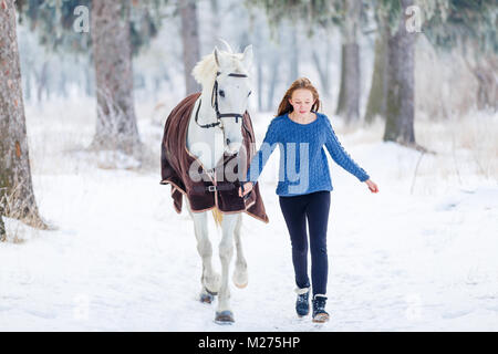 Giovane ragazza adolescente a piedi con il suo cavallo bianco in winter park Foto Stock