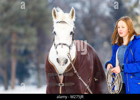 Giovane ragazza adolescente a piedi con il suo cavallo bianco in winter park Foto Stock