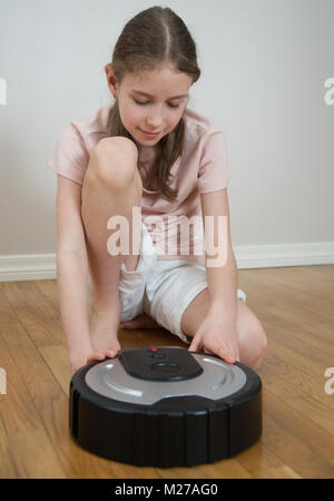 Bambina e robot aspirapolvere sul pavimento. Foto Stock