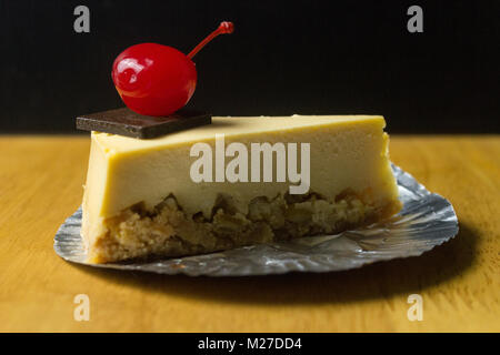 Pezzo di cheesecake con la ciliegia sulla tavola di legno e uno sfondo scuro Foto Stock