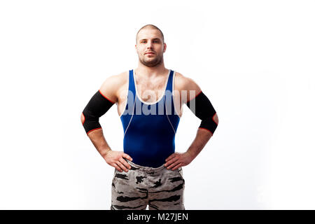 Atletica Giovane wrestler maschio in maglietta blu, sport pantaloni ed elbow pads in piedi con le mani sulla cintura bianca su sfondo isolato Foto Stock