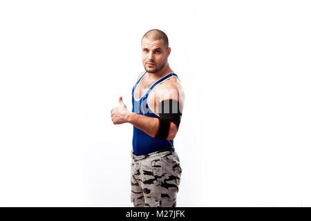 Atletica Giovane wrestler maschio in maglietta blu, sport pantaloni ed elbow pads sorge e mostra il pollice fino a White background isolato, vista laterale Foto Stock