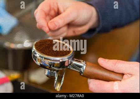 Barista il riempimento di una maniglia per caffè con caffè Grind prima di prendere una tazza di caffè usando una normale macchina da caffè di close-up. Foto Stock