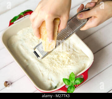 Parmigiano grattugiato chesse sui cannelloni pasta con basilico sulla luce sfondo di legno Foto Stock