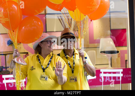 Due volontari sorridente in magliette di colore giallo arancio holding palloncini a Marlyebone Estate Fayre Marlyebone Food Festival a Londra in una giornata di sole Foto Stock