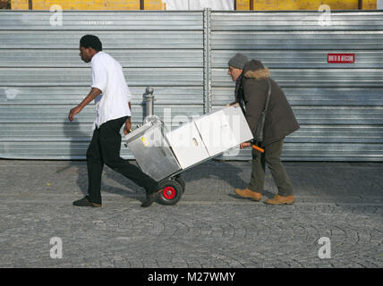 Gli uomini tirando il carrello caricato sulla strada, Milano, Italia Foto Stock