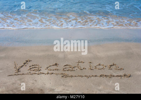 Concetto di vacanza : scrittura le parole 'vacanza' sulla spiaggia di sabbia bianca con onde del mare blu in background. Foto Stock