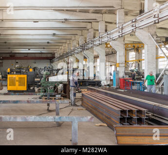 Un lavoratore in un negozio di macchine utensili per la lavorazione di metalli. Un uomo taglia profilo smerigliatrice in metallo Foto Stock