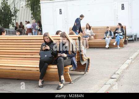 Mosca, Russia - 21 giugno 2017 ragazze con i capelli lunghi seduto su una panchina nel parco e guardare il telefono cellulare Foto Stock