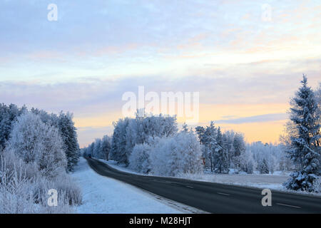 Autostrada rurale in inverno tramonto con il cielo al tramonto e trasformata per forte gradiente frost alberi coperti. Foto Stock
