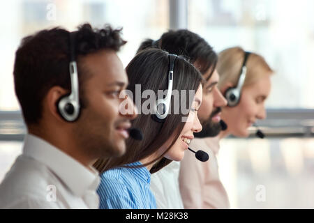 Ragazza asiatica con cuffia a lavorare in una società. Focalizzato call center operatore seduto nella fila di colleghi in ufficio. Finestre luminose sullo sfondo. Foto Stock