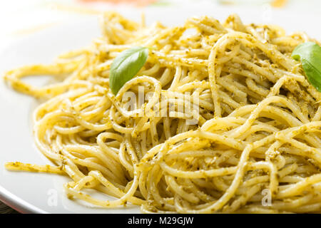 Spaghetti con fatti in casa al pesto di olio di oliva con le foglie di basilico sulla piastra bianca Foto Stock