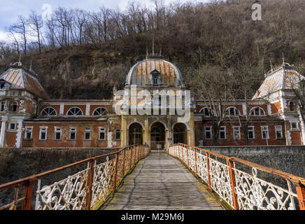 Baile Herculane, Romania - 01.01.2018: ponte che attraversa il fiume Cerna e conduce ad un edificio abbandonato del vecchio Asburgo bagni Imperiali Foto Stock