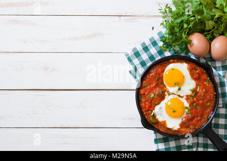 Colazione messicana: Huevos rancheros in ferro padella su bianco tavolo in legno vista superiore Foto Stock