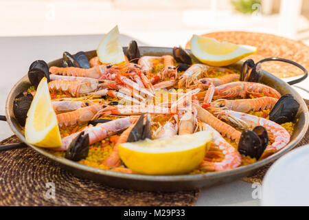 La paella spagnola servita sulla tradizionale teglia per essere goduto sotto un'ombra su una soleggiata giornata estiva. Foto Stock