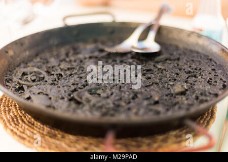 Nero spagnolo paella servita sulla tradizionale teglia per essere goduto sotto un'ombra su una soleggiata giornata estiva. Foto Stock