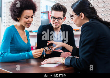 Donna e uomo acquisto di bicchieri a ottico store ricevendo consigli da saleslady Foto Stock