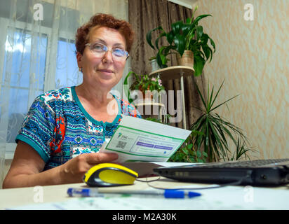 Voronezh, Russia - Giugno 19, 2016: donna anziana tenendo un ricevimento e sta andando a pagare per essa nella banca online Foto Stock