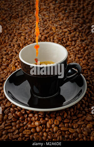 Il versamento di caffè verso il basso in una tazza, su un letto di chicchi di caffè Foto Stock