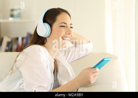 Felice ragazza guarda lontano ascoltando la musica seduto su un divano nel salotto di casa Foto Stock