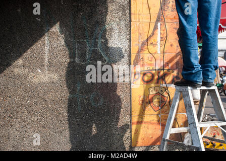 Un uomo in piedi su una scala che indossa jeans durante la riparazione dei cablaggi Foto Stock