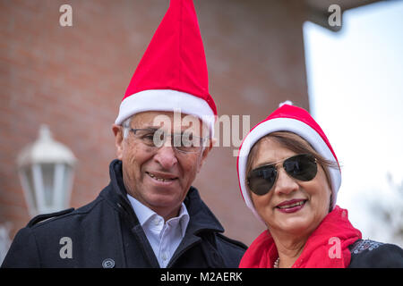 Senior coppia sposata si pongono con un papa noel cap nel giardino della loro casa Foto Stock