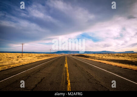 Un taglio di autostrada tra golden pascolo con montagne in distanza sotto un cielo nuvoloso in Colorado paesaggio di campagna Foto Stock