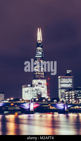 Londra - Febbraio 01, 2018: colpo verticale di Shard edificio sul moderno skyline di Londra con luci e riflessioni sul Fiume Tamigi di notte Foto Stock