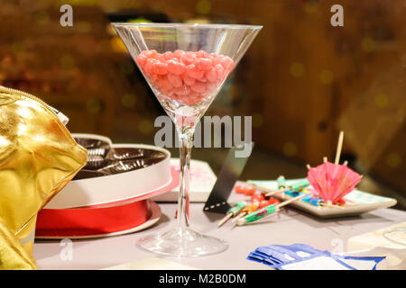 Martini di vetro riempita con jellybeans rosa sul tavolo con bevanda diffusa ombrelloni e quasi vuoto di cioccolato di san valentino - scatola di fuoco selettivo Foto Stock
