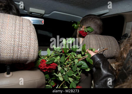 Night Shot di interni auto con una donna tenendo fuori un mazzo di rose al passeggero maschio che ha una rosa dietro il suo orecchio Foto Stock