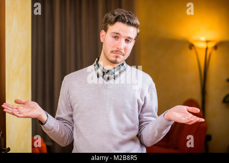 Confuso o dubbia giovane uomo scrollare con palme aperte Foto Stock