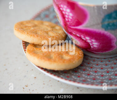 In prossimità dei due round biscotti su un piattino - abbastanza motivi floreali cup - sfondo beige Foto Stock