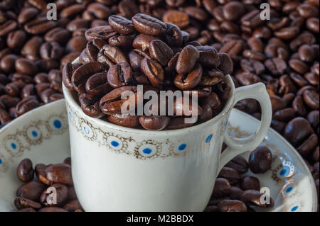 Tazza e piattino pieno di chicchi di caffè su un chicco di caffè sfondo concetto espresso con spazio copia di close-up. Foto Stock