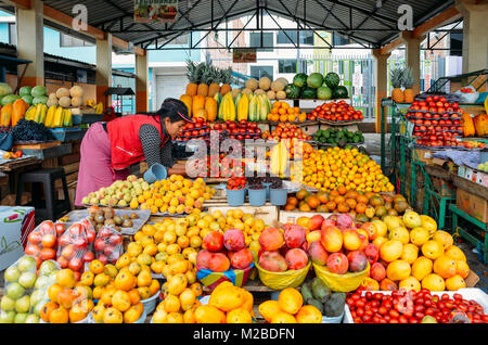 Ambato, Ecuador, Dicembre 20, 2017: donna ecuadoriana fruttivendola di fronte a lei visualizza di frutti tropicali in un mercato Foto Stock