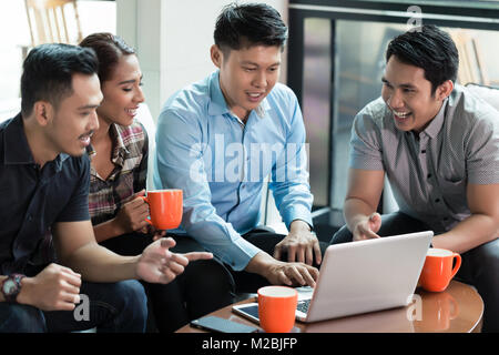 Due cinesi allegro giovani uomini usando un computer portatile durante la condivisione di idee di business con i loro colleghi durante il lavoro per il successo di una società multinazionale Foto Stock