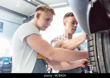 A basso angolo di vista di un tecnico meccanico automatico lavorando insieme con il suo collega alla messa a punto di un auto in una moderna automobile repair shop, con affidabili Foto Stock