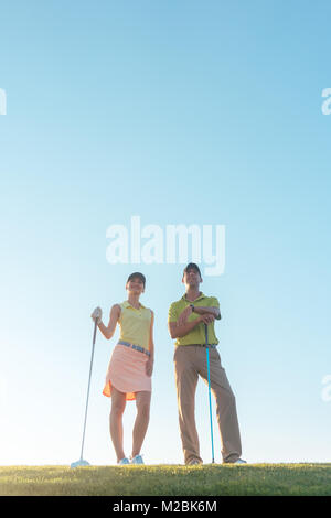 A basso angolo di visione della silhouette di un uomo rivolto verso l'orizzonte, mentre in piedi accanto al suo partner femmina su un campo di golf professionale contro il sole Foto Stock