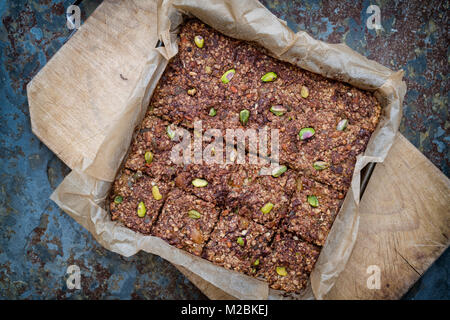 In casa di sementi, dado, frutta secca e cioccolato fondente Oat barrette energetiche sulla carta da forno su sfondo di ardesia Foto Stock