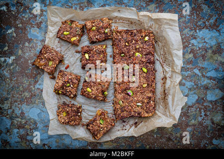 In casa di sementi, dado, frutta secca e cioccolato fondente Oat barrette energetiche sulla carta da forno su sfondo di ardesia Foto Stock