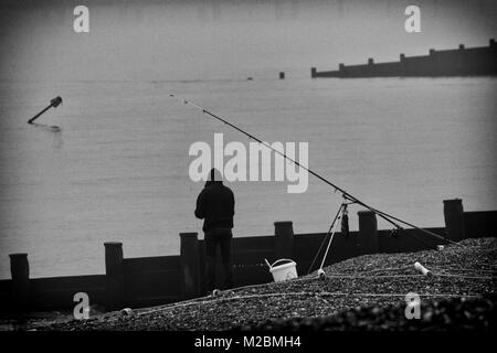 Lone pescatore sulla spiaggia in inverno su una spiaggia del Regno Unito, in bianco e nero Foto Stock