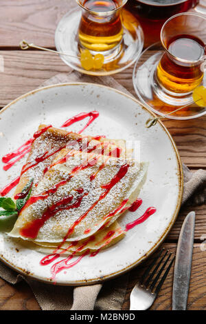 Deliziose frittelle sottili servito con salsa di fragole su un di legno tavolo rustico Foto Stock